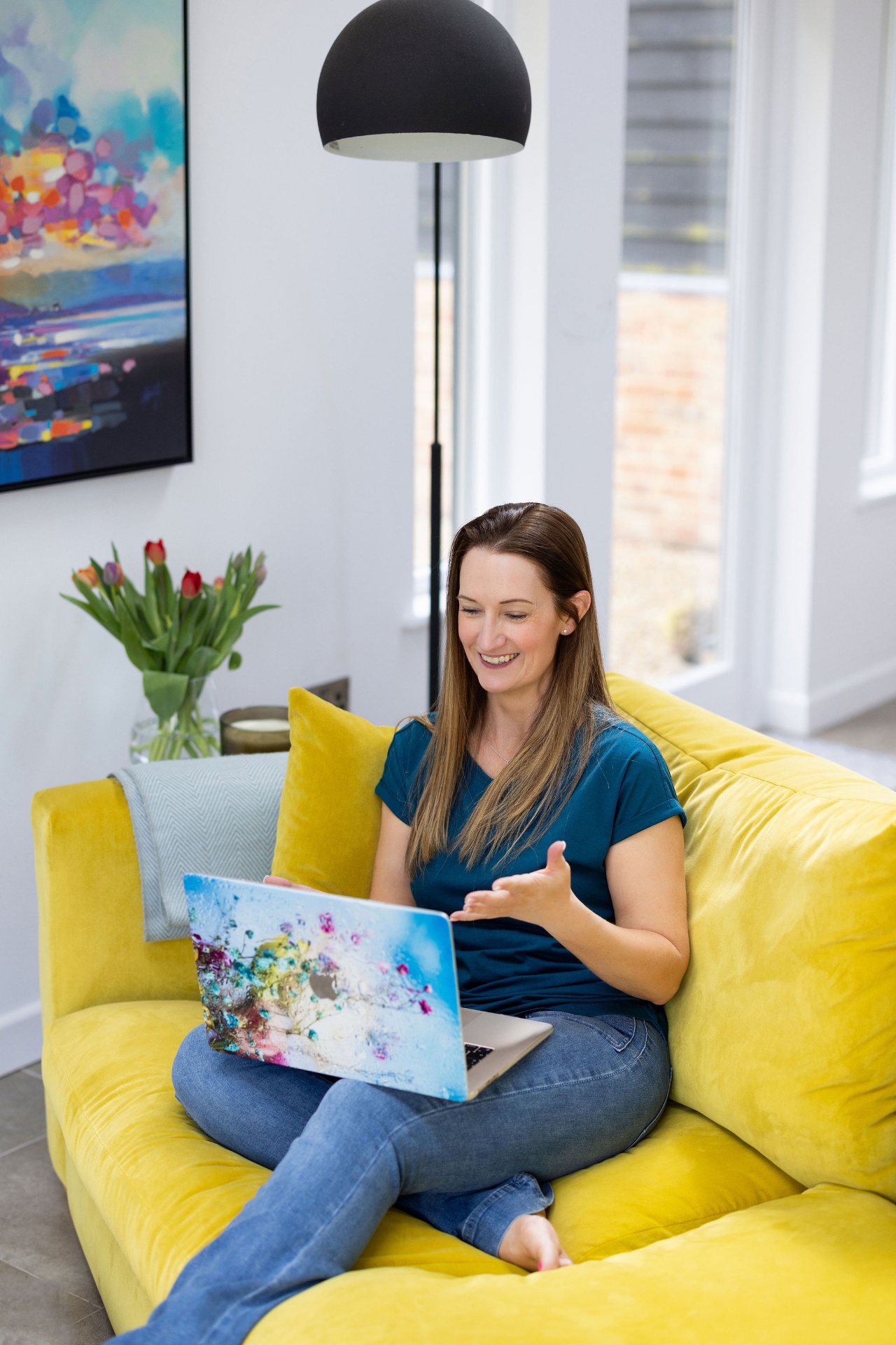 Emma smiling at her laptop on a yellow sofa